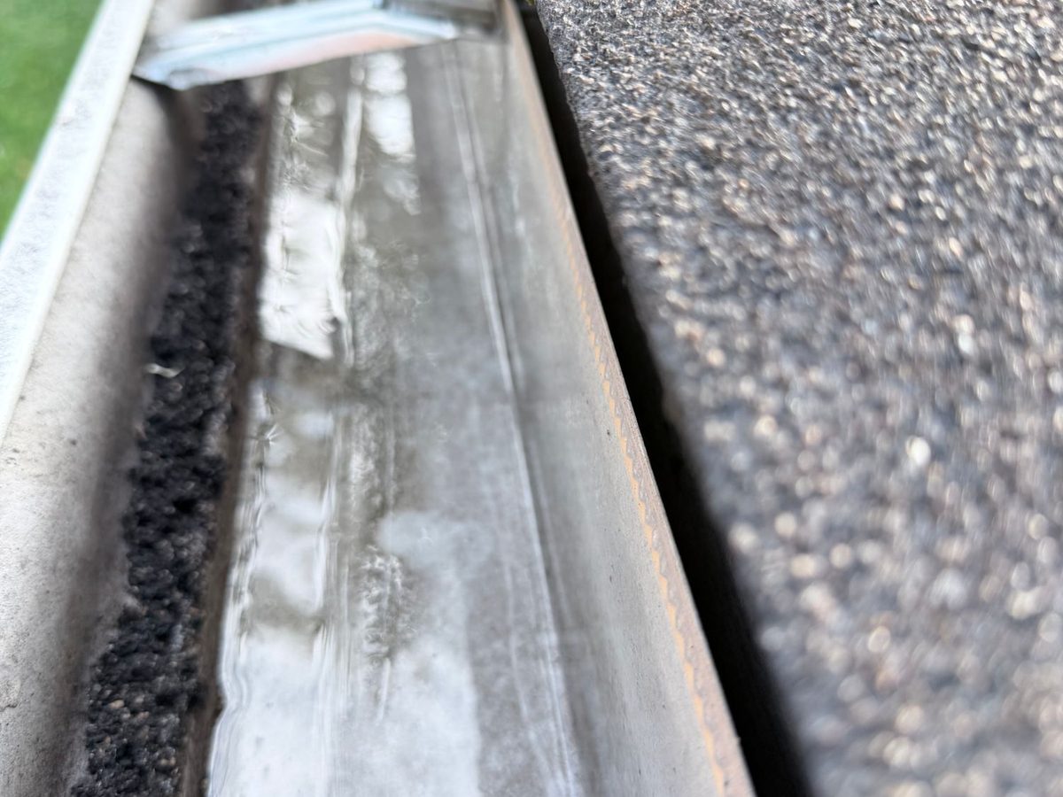A cleaned gutter with rinse water running along the bottom toward the downspout