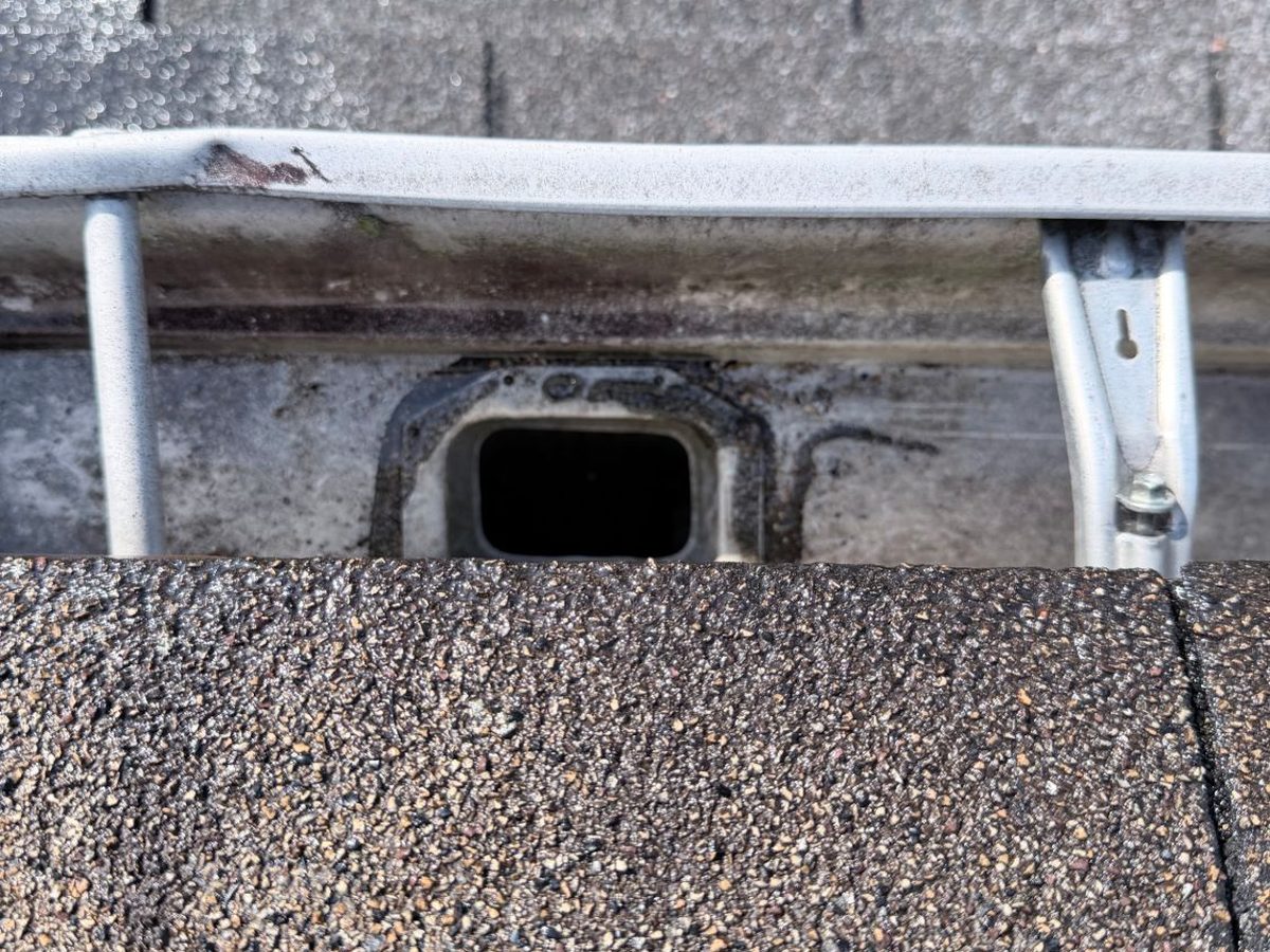 Looking down at a clean, open downspout outlet in a gutter after cleaning