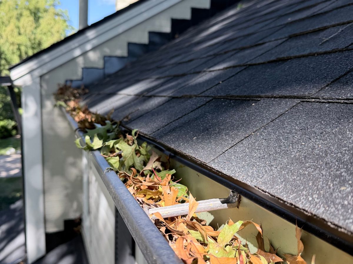 Leaves piled in a gutter corner below a gable end before cleaning