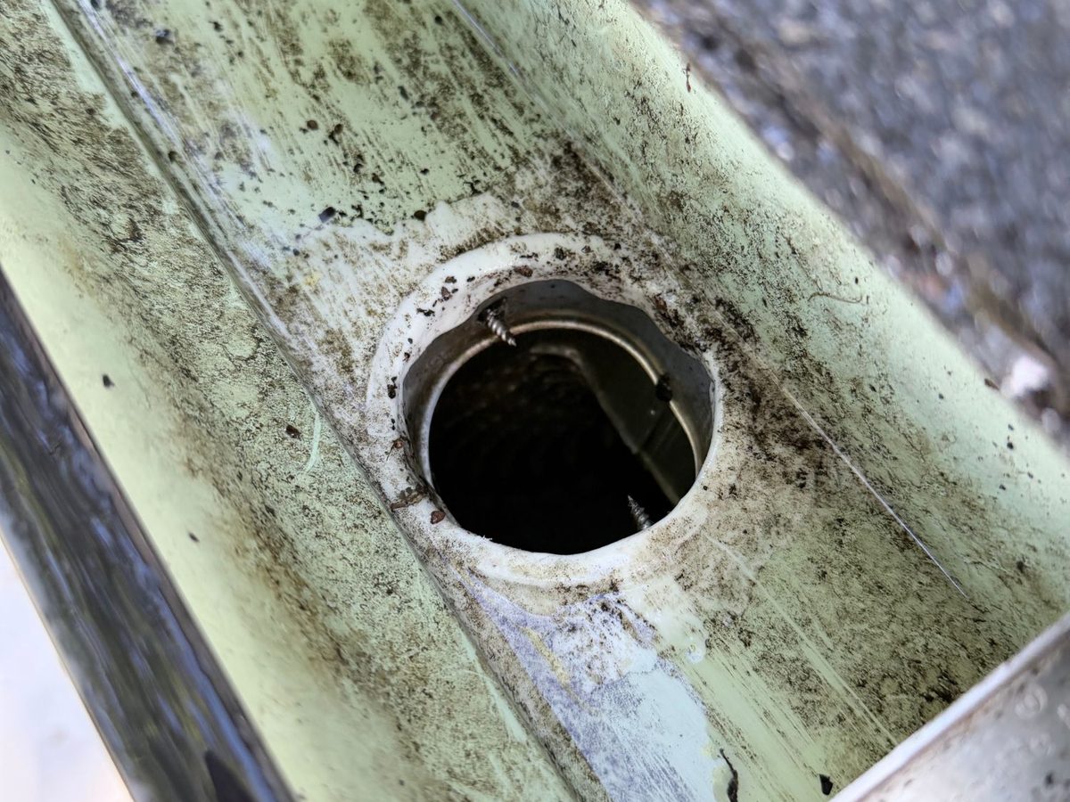 Close-up of a downspout outlet cleared of debris after a hand cleanout and flush