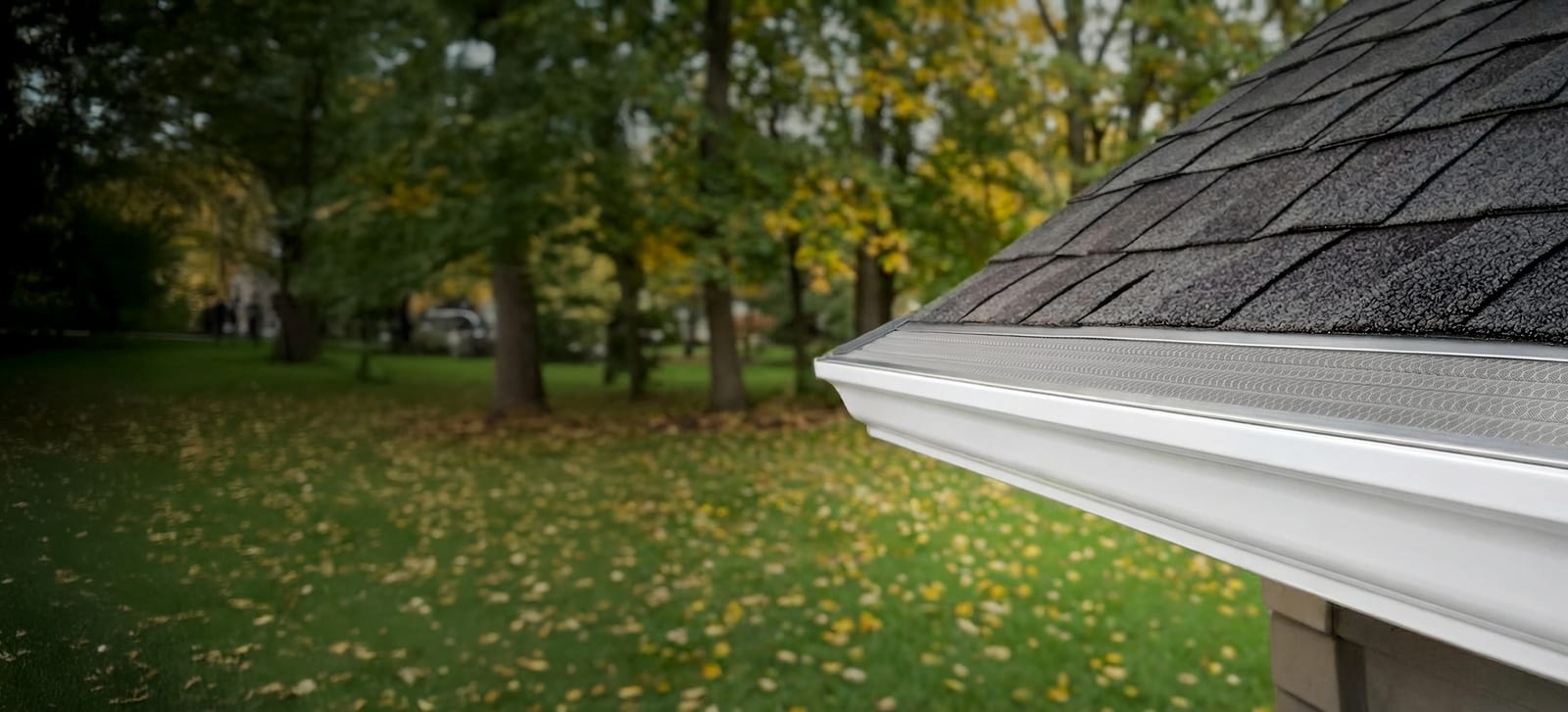 Leaf Solution gutter guard installed on a white gutter with fall leaves on the lawn behind