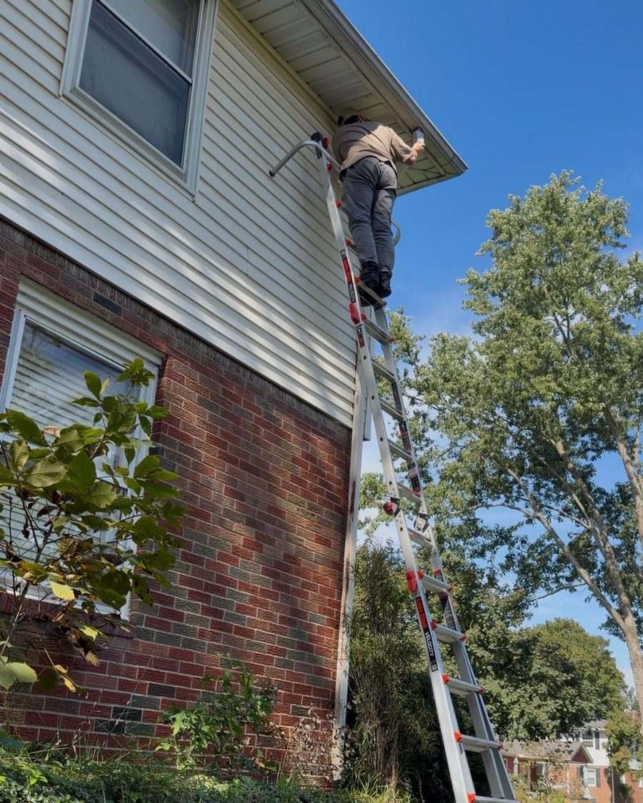 Christian Schaffner of Guttrz on a ladder with a standoff, clearing the top of a downspout at a two-story house